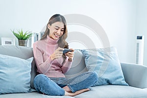 Asian young beautiful woman playing mobile game on smartphone at home. Attractive casual girl feel happy and relax, sit on sofa