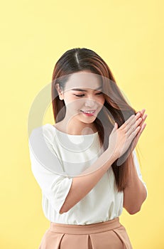 Asian young beautiful woman smiling and touching smooth her hair on yellow background