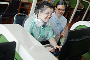 Asian young blind woman with headphone using computer with braille display assistive device discusing with senior colleague woman