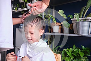 Asian young boy getting a haircut at home, Father makes a haircut for his son with scissors. Home haircut while in quarantine