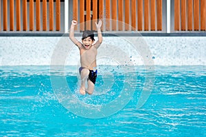 Asian Young Boy Having a good time in swimming pool, He Jumping and Playing a Water in Summer