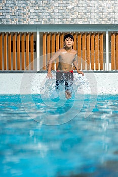 Asian Young Boy Having a good time in swimming pool, He Jumping and Playing a Water in Summer