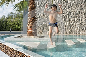 Asian Young Boy Having a good time in swimming pool, He Jumping and Playing a Water in Summer