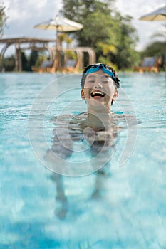 Asian Young Boy Having a good time in swimming pool, He Jumping and Playing a Water in Summer