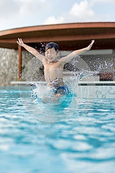 Asian Young Boy Having a good time in swimming pool, He Jumping and Playing a Water in Summer