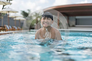 Asian Young Boy Having a good time in swimming pool, He Jumping and Playing a Water in Summer