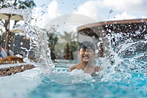 Asian Young Boy Having a good time in swimming pool, He Jumping and Playing a Water in Summer