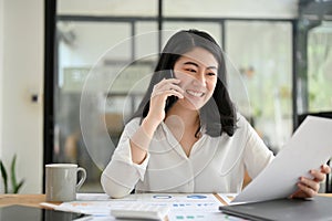 Asian young businesswoman talking on the phone while looking the details on her report