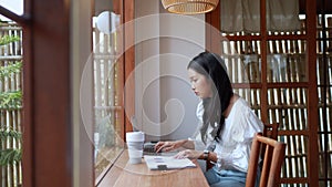 An Asian young businesswoman is working at a nearby cafe, using her laptop