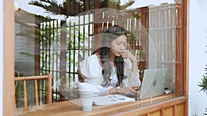 An Asian young businesswoman is working at a nearby cafe, using her laptop