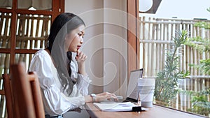 An Asian young businesswoman is working at a nearby cafe, using her laptop