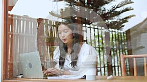 An Asian young businesswoman is working at a nearby cafe, using her laptop