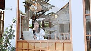 An Asian young businesswoman is working at a nearby cafe, using her laptop