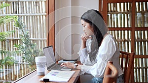 An Asian young businesswoman is working at a nearby cafe, using her laptop