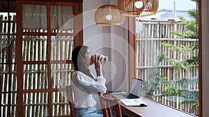 An Asian young businesswoman is working at a nearby cafe, using her laptop