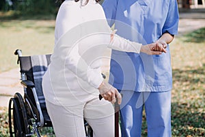 Asian young caregiver nurse support senior older male walking outdoors. Specialist girl doctor help and take care of elderly