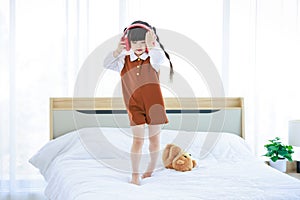 Asian young cheerful happy little cute daughter girl standing wearing red wireless stereo headset listening to online music dancin