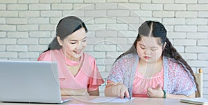 Asian young chubby down syndrome autistic daughter learning mathematic lesson from happy mother via laptop computer at home.