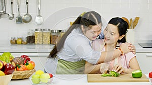 Asian young chubby down syndrome autistic daughter wears apron hugging cuddling showing love to mother sitting cutting sweet