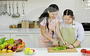 Asian young chubby down syndrome autistic daughter wears apron hugging cuddling showing love to mother sitting cutting sweet