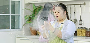 Asian young chubby down syndrome autistic daughter wears apron learning baking bakery dessert threshing flour by hands and rolling