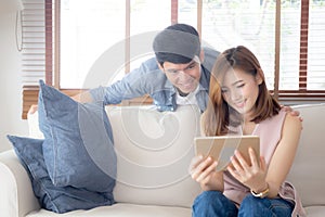 Asian young couple relax looking tablet entertainment on internet together on sofa at home