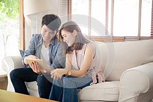 Asian young couple relax looking tablet entertainment on internet together on sofa at home