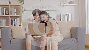 Asian young couple sit on couch or sofa looking at Computer Laptop smile and laughing together. Cheerful lover surfing internet
