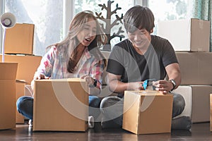 Asian young couple unpack cardboard box after moving in new house