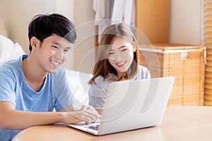 Asian young couple using laptop computer think and searching internet together, man and woman casual smiling work