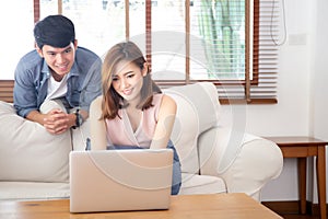 Asian young couple using laptop computer think and searching internet together, man and woman casual smiling work at home