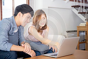 Asian young couple using laptop computer think and searching internet together, man and woman casual smiling work at home