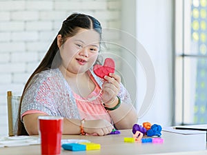 Asian young cute fun chubby down syndrome autistic female art artist student wearing eyeglasses sitting smiling at table holding