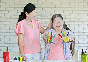 Asian young cute happy chubby down syndrome autistic daughter showing colorful painted hands smiling look at camera while mom