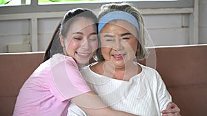 asian young daughter hug and kissing her senior mother on sofa at home . young woman embrace old mom to take care