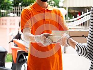 Asian young delivery man holding pizza box cardboard by express service while wearing orange polo shirt uniform and face mask