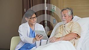 Asian young doctor using digital tablet explain the symptoms to the patient after treatment or Talking With old man patient on bed