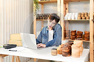 Asian young entrepreneur guy using mobile to calling confirm order and typing keyboard on laptop for check product stock online on