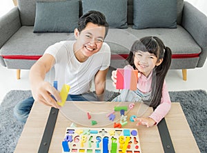 Asian young father and daughter indoors sit on floor playing with toy and smiling