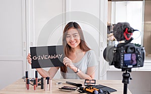 Asian young female blogger giveaway gift to fan following channel while recording vlog video with makeup cosmetic at home online photo