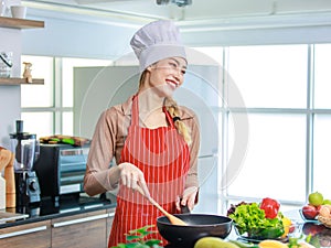 Asian young female chef wears white tall cook hat and apron smiling posing ready to cooking food with pan at counter with bread