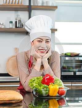 Asian young female chef wears white tall cook hat and apron smiling posing ready to cooking food with pan at counter with bread