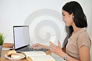 Asian young female college student using notebook laptop and holding a cup of coffee