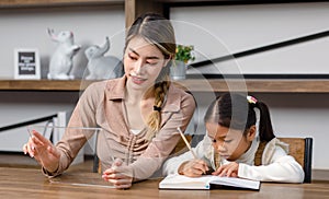 Asian young female housewife mother tutor teacher sitting smiling on table in living room holding tablet computer pointing