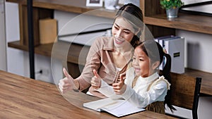 Asian young female housewife mother tutor teacher sitting smiling on table in living room at home teaching little cute