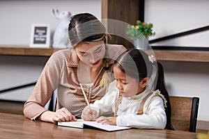 Asian young female housewife mother tutor teacher sitting smiling on table in living room at home teaching little cute