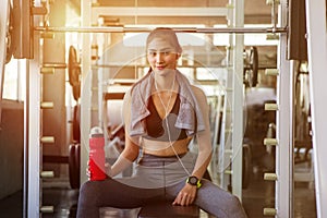 asian young fitness woman with towel listening music with earphones holding water bottle relaxing sitting on Weight lifting