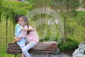 Asian young girl child embracing little boy while sitting on wooden bench in the park