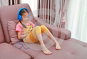 Asian young girl child wearing headphone and using smartphone on sofa in living room at home