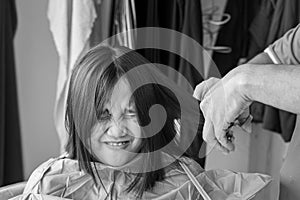 Asian young girl  with funny expression is getting haircut at home from the father. Young teenage girl. Monochrome, black and